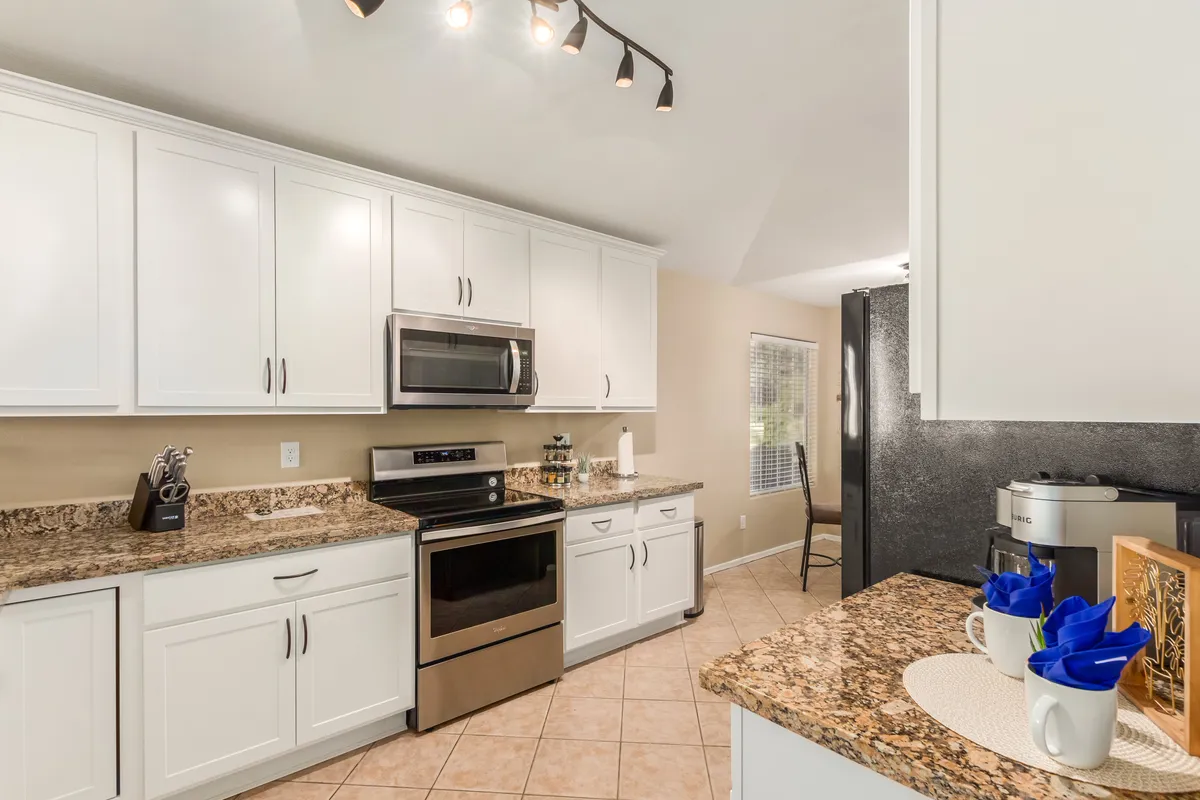 A bright, open-concept kitchen and dining area featuring sleek granite countertops, modern stainless steel appliances, white cabinetry, and a welcoming dining space. The scene is set for both culinary creativity and shared meals, with ample prep space and inviting design touches.