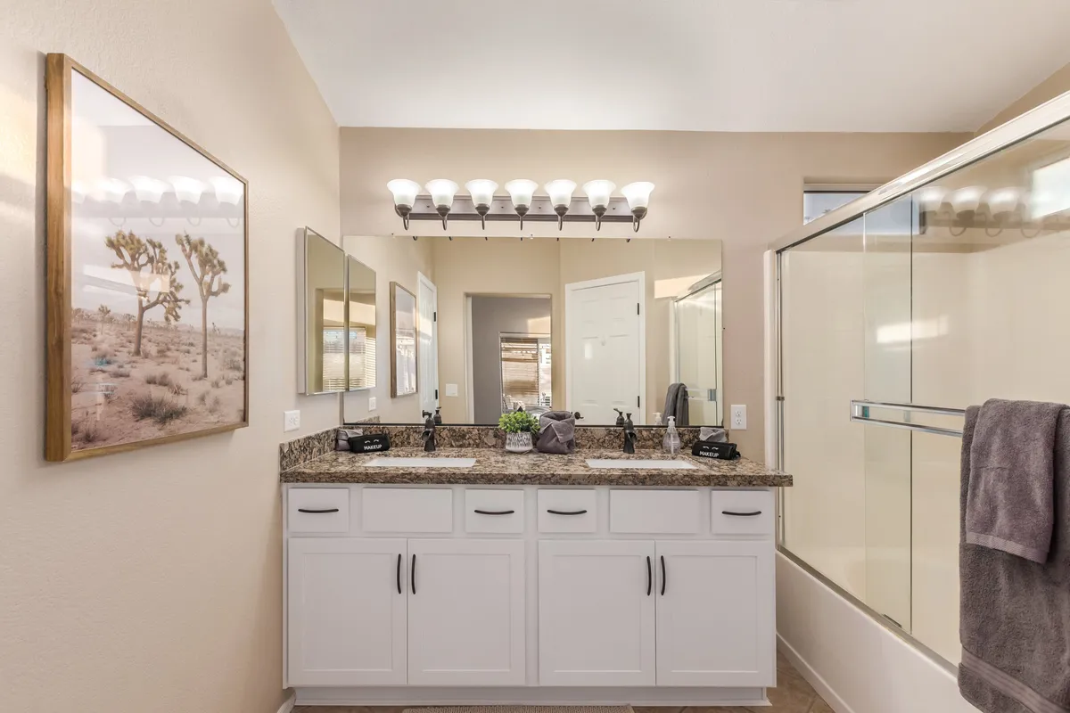 A modern bathroom with a granite countertop, large mirrors, framed desert-themed artwork, and sleek light fixtures. The overall ambiance is inviting and serene, perfect for self-care and unwinding.