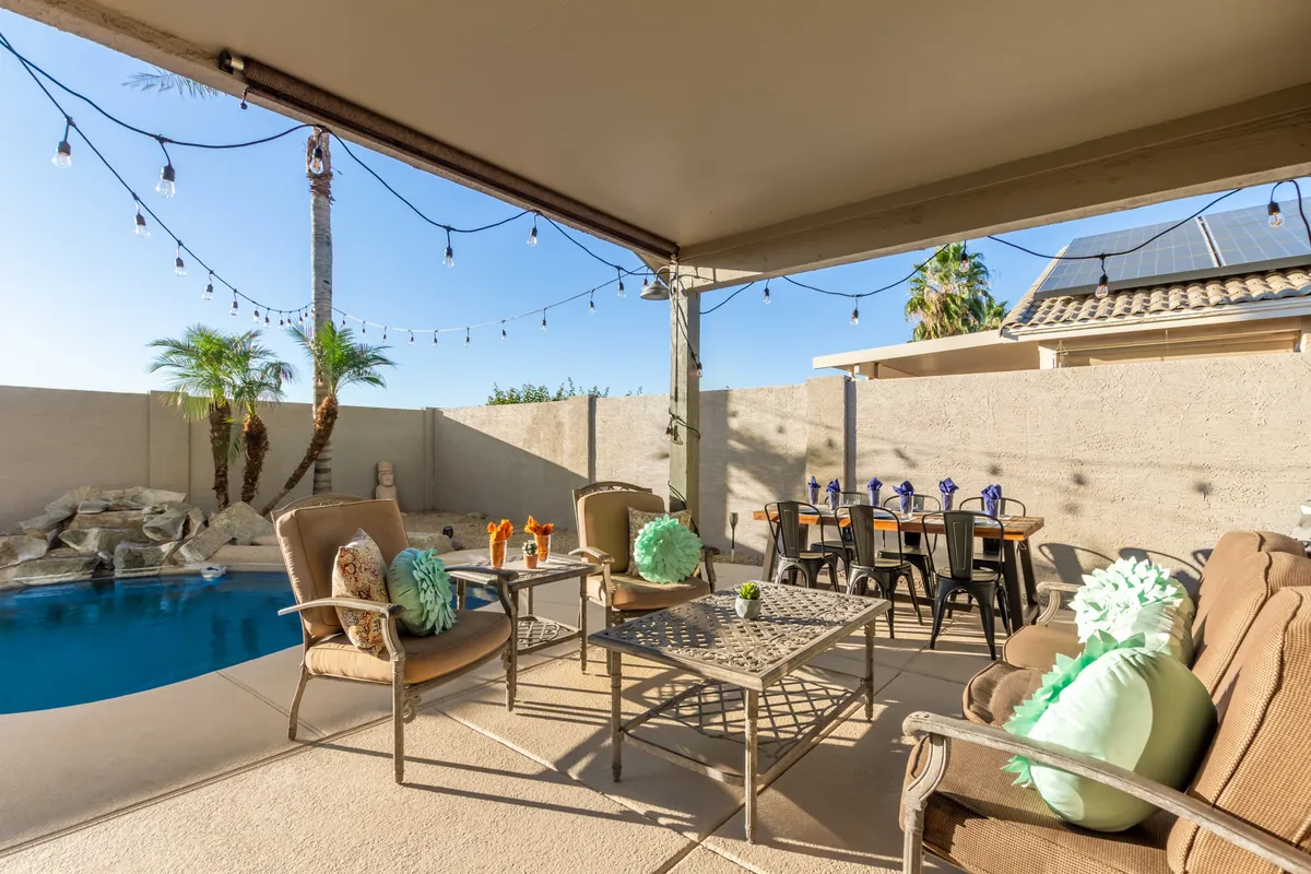 A cheerful outdoor scene featuring a pool, ample seating, decorative pillows, and string lights overhead. The setup is ideal for group dining, lively conversation, and relaxing by the water in a festive, welcoming environment.