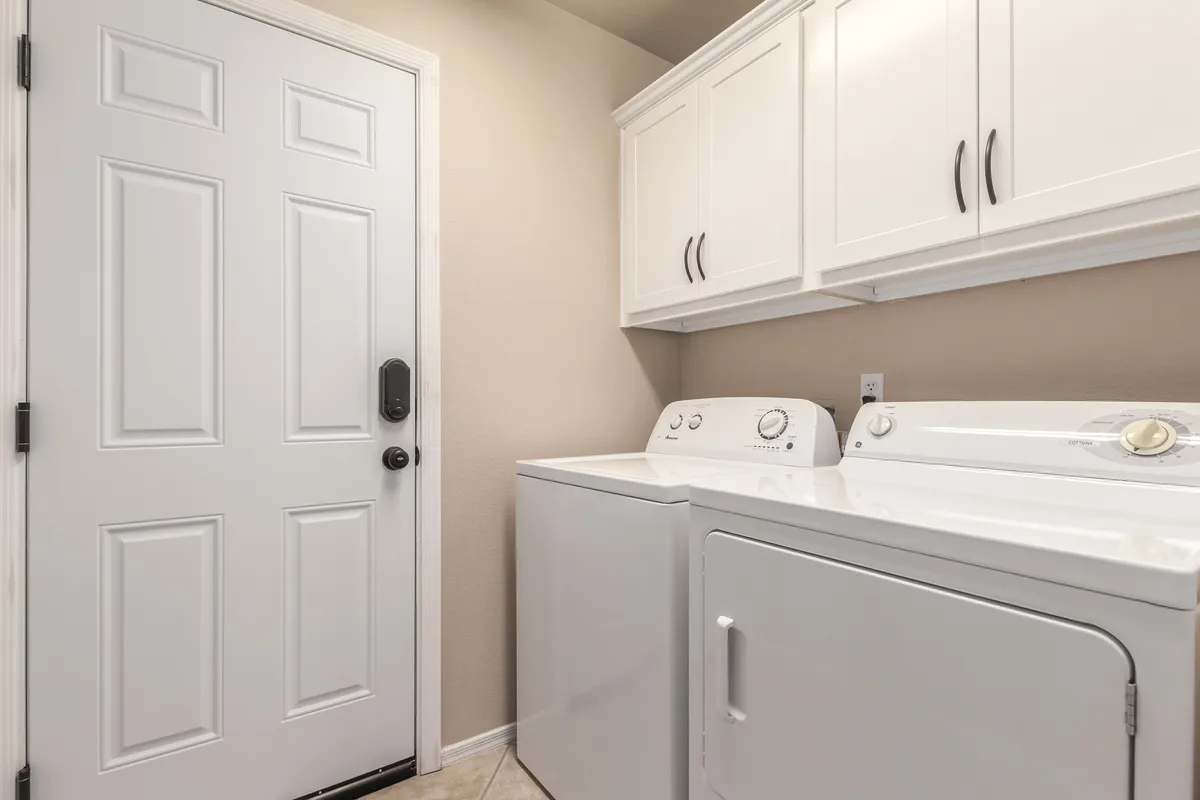 A well-organized laundry area featuring a washer, dryer, storage cabinets, and a door, set in a practical and tidy interior space. The clean lines and uncluttered look emphasize the utility and comfort of at-home laundry facilities.