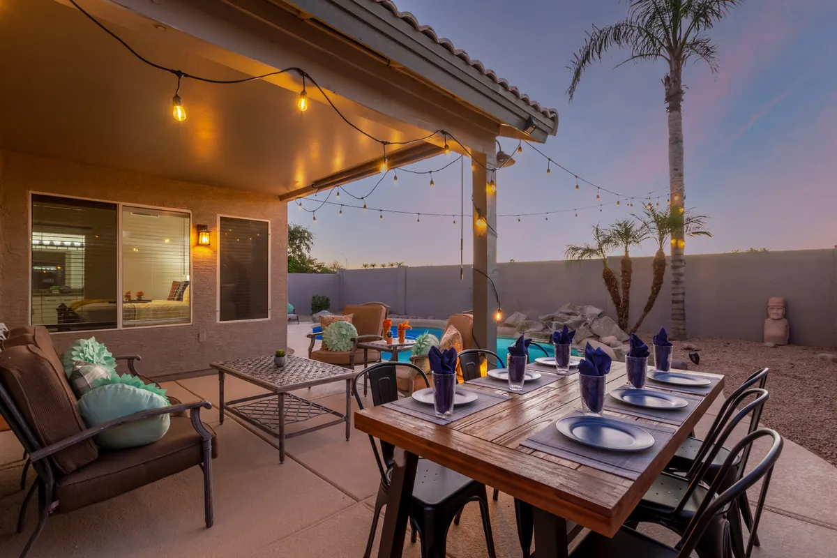 This scene features a well-set outdoor dining table under overhead string lights, with the pool and palm trees in the background. The comfortable seating and festive table setting create a welcoming environment for al fresco dining, evening celebrations, or peaceful morning coffee.