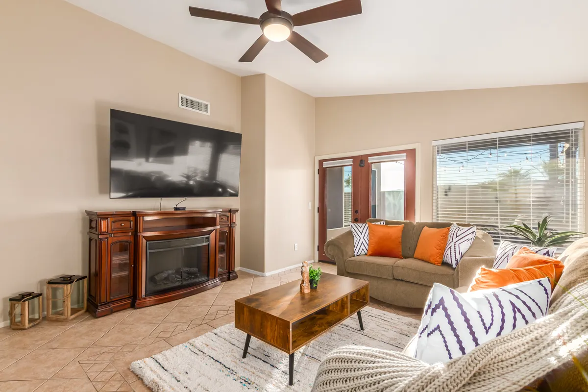 A cozy living room setting featuring a large flat-screen TV, a wooden coffee table, and a plush couch adorned with colorful cushions. The space radiates comfort and is clearly designed for movie nights, family gatherings, or relaxed evenings by the fire.