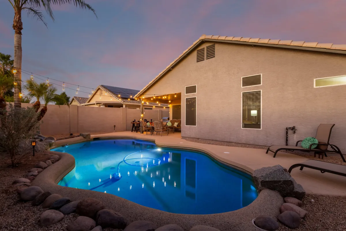 A sparkling swimming pool is surrounded by an outdoor seating area, string lights draped overhead, and inviting lounge furniture. The ambiance is relaxed, perfect for sunset swims, dining al fresco, and socializing with friends under the stars.